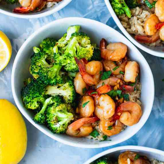 close view of a bowl of honey garlic shrimp and roasted broccoli on top of miso brown rice.