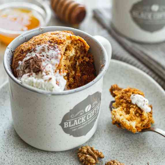 A honey cake in a mug. A scoop is taken out on a spoon. 