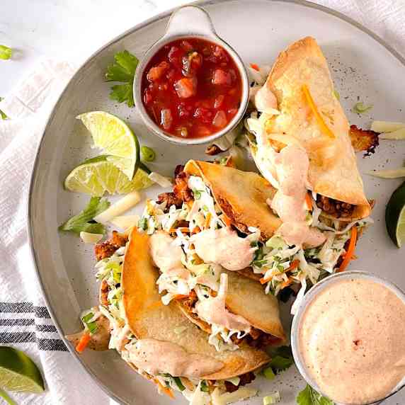 Four crispy tacos stuffed with turkey and slaw, arranged on a plate next to bowls of sauce.