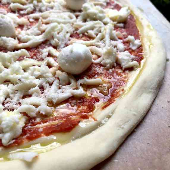 Closeup of an unbaked assembled thick crust pizza with mozzarella and mini buffalo mozzarella balls.