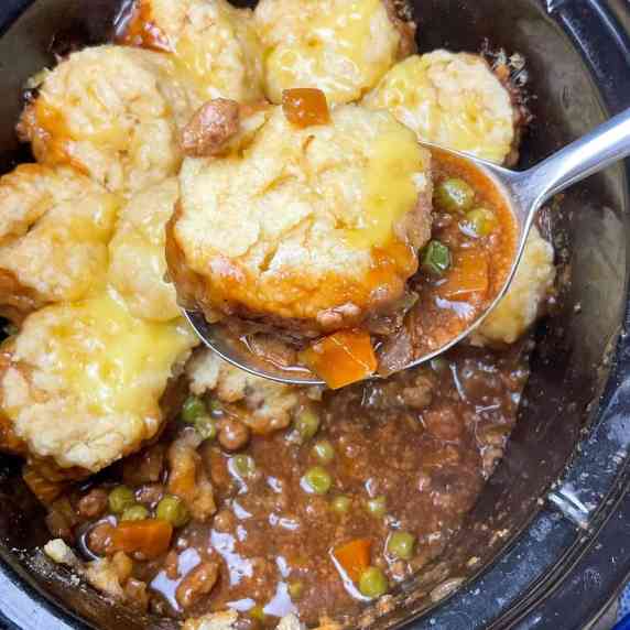 Slow cooker pot with savoury mince cobbler and serving spoon scooping a portion out.