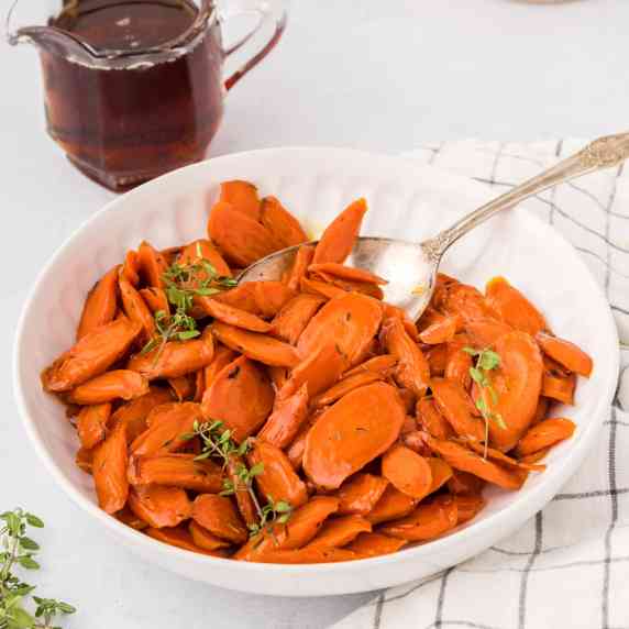 Maple glazed carrots garnished with thyme in a serving bowl with a spoon