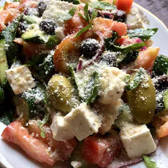A platter of Greek salad with cubed feta, tomatoes, huge green olives, black olives, and cucumbers.