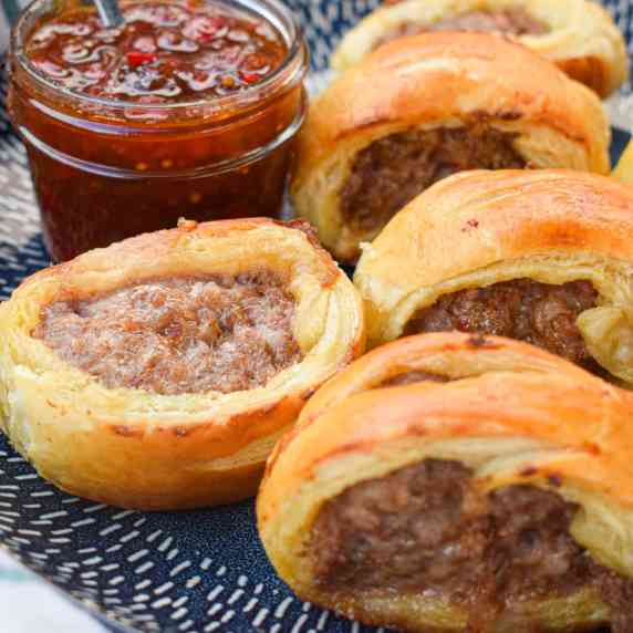 Puff pastry sausage rolls on a blue plate with tomato chutney in a mason jar