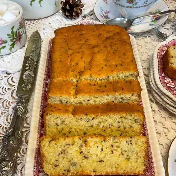 A seed cake on a serving tray with silver knife to side, tea cup and saucer, sugar bowl to side.