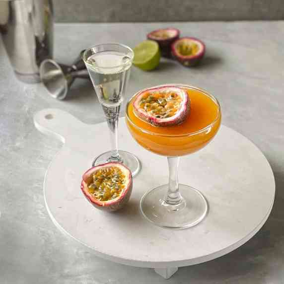 a passion fruit cocktail on a tray with a shot of sparkling wine and passion fruit half.