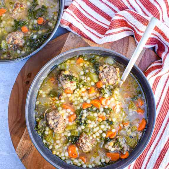 Black bowl of Italian wedding soup with meatballs, carrots, celery and cous cous in a broth. 