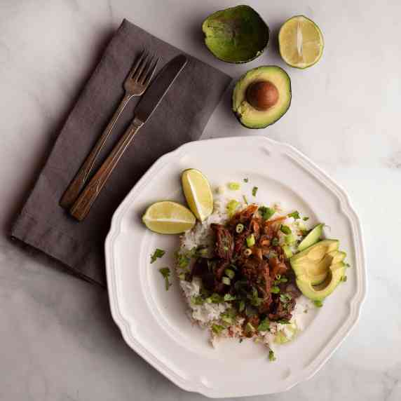 Mexican Beef Stew served on rice with limes and avocados 