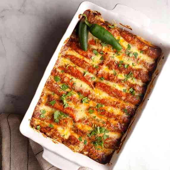 A 9x13 baking dish filled with From Scratch Chicken Enchiladas garnished with cilantro and peppers.