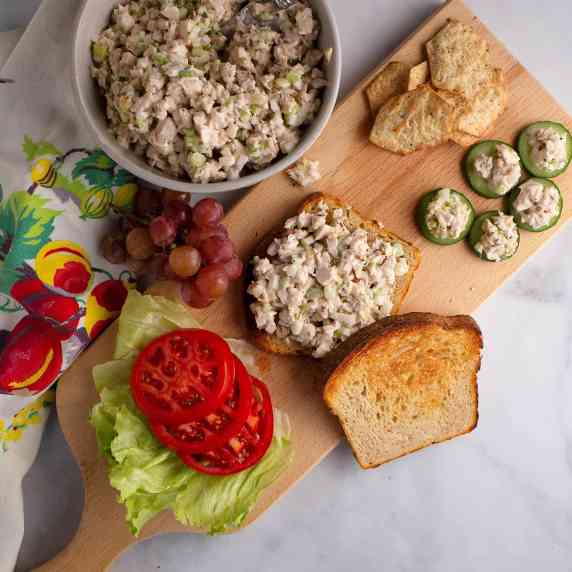 A bowl of chicken salad, a sandwich with chicken salad, tomato slices, and lettuce, cucumber rounds