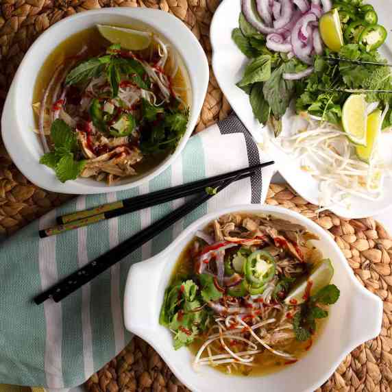 Two bowls of Vietnamese Chicken Pho with condiments and chopsticks.