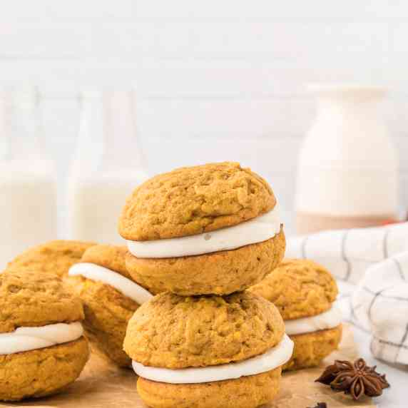 stacked pumpkin whoopie pies surrounded by more pumpkin whoopie pies on brown parchment paper