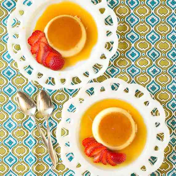 Two individual servings of flan on vintage milkglass dessert plates, garnished with strawberries