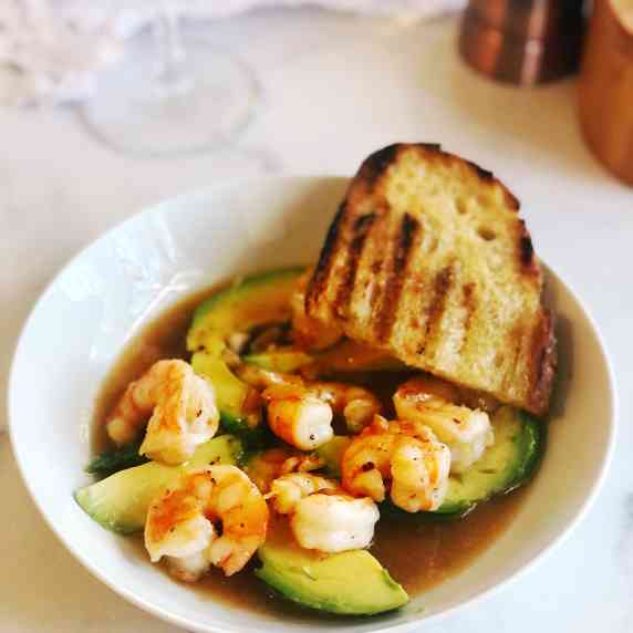 shrimp and avocado in a bowl with bread on the side.