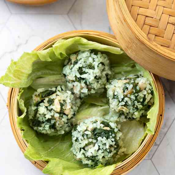Four vegan meatballs coated in jade pearl rice in bamboo steamer.