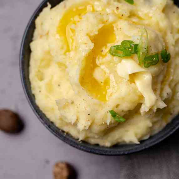 top down view on bowl of mashed potatoes, garnished with melted butter and green onion