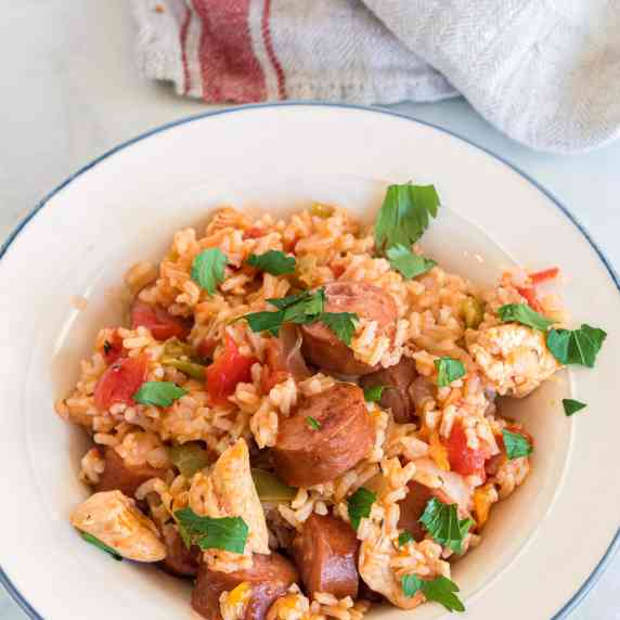 Chicken, sausage, peppers and rice topped with parsley in a white bowl