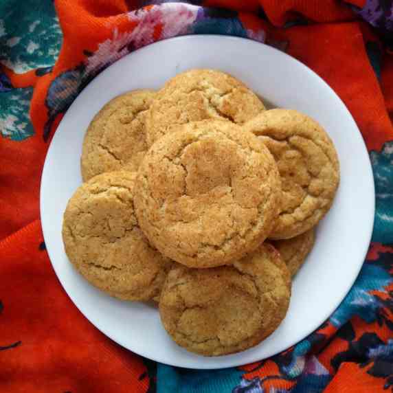 Chai spice snickerdoodle cookies arranged on a white plate on top of orange floral fabric.