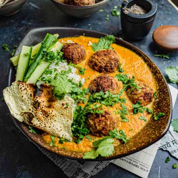 Lauki kofta with rice, cucumber, and papad in a brown bowl.