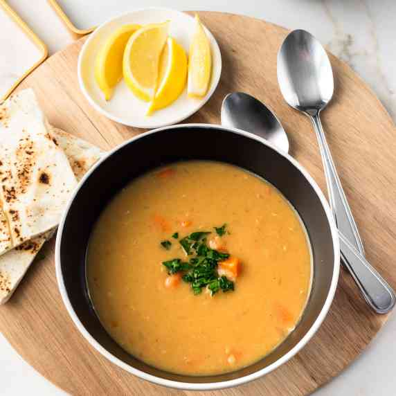 Bowl of red lentil soup served with pita bread and lemon wedges. 