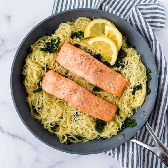 Lemon Kale Pasta with Salmon in a skillet with some lemon wedges.