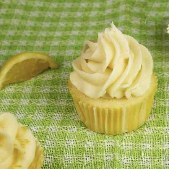 A lemon cupcake with creamy white buttercream frosting sits on a green and white plaid cloth.