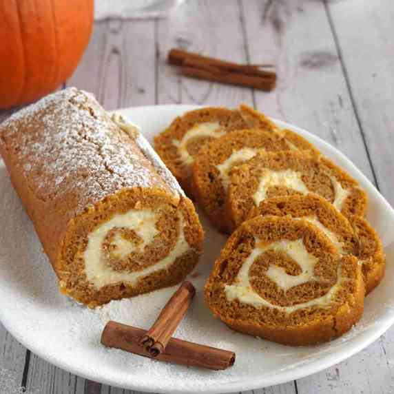 Libby's pumpkin roll and slices on a plate with cinnamon sticks and a pumpkin in the background
