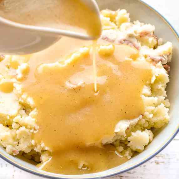 gravy pouring out of a gravy boat onto mashed potatoes.