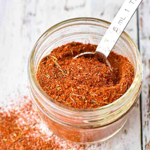 a clear jar of homemade cajun seasoning mix with a teaspoon on a white background