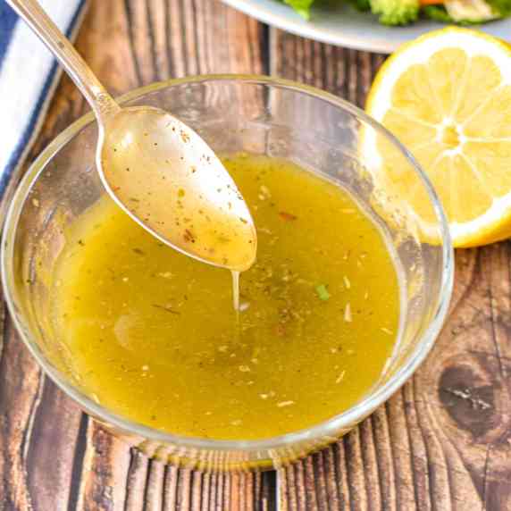 a spoon pouring low fodmap italian dressing into a glass bowl on a wooden background