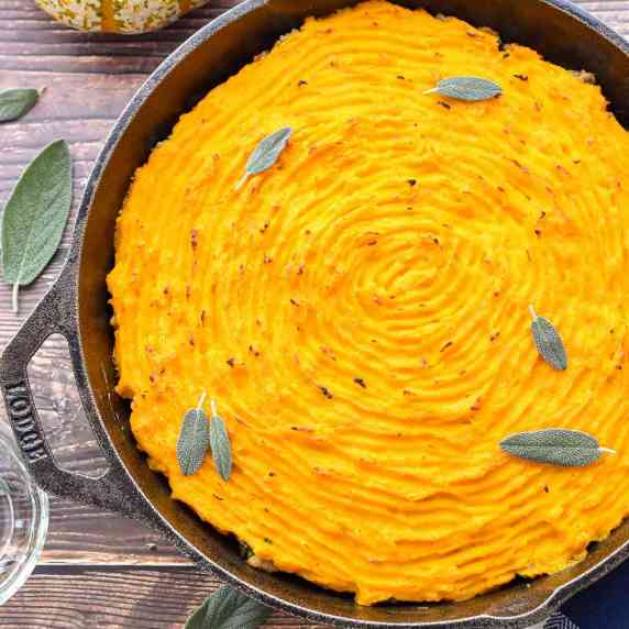 shepherd's pie with a squash topping garnished with sage leaves in a cast iron skillet.