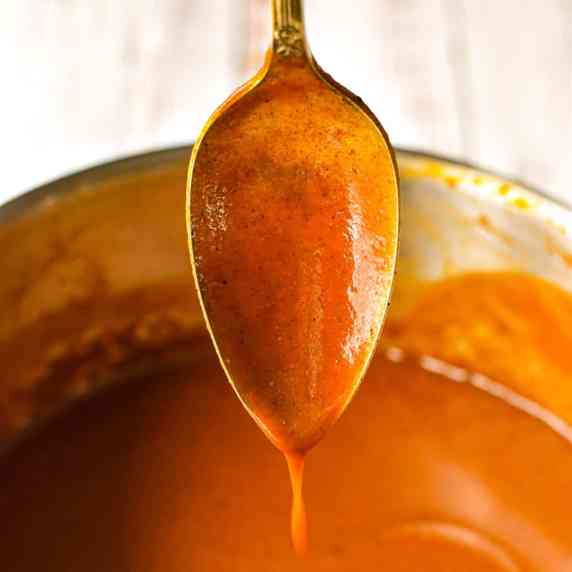 a spoon dripping with enchilada sauce into a saucepan
