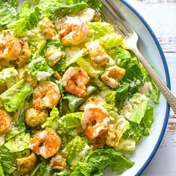 a dressed low fodmap shrimp caesar salad on a blue and white plate with a fork