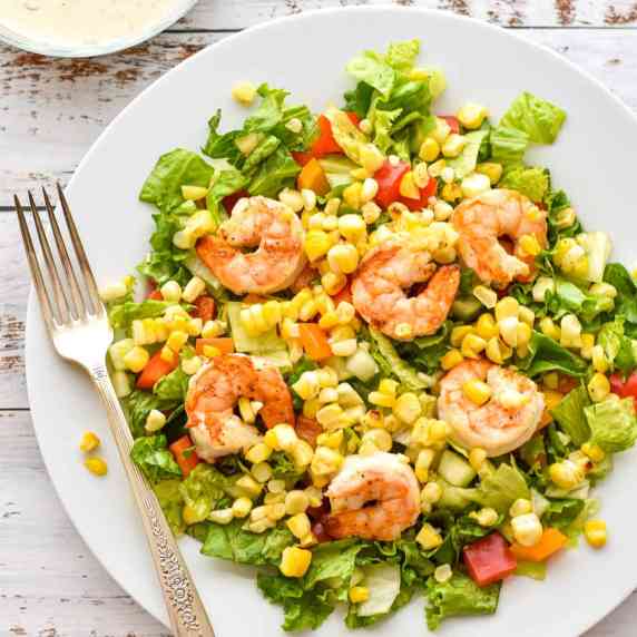 salad with shrimp and corn on a white plate with a fork in front of a bowl of ranch dressing