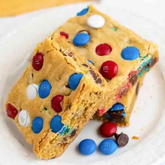 Stack MM cookie bars on plate from side with more red white and blue MMs next to the bars.