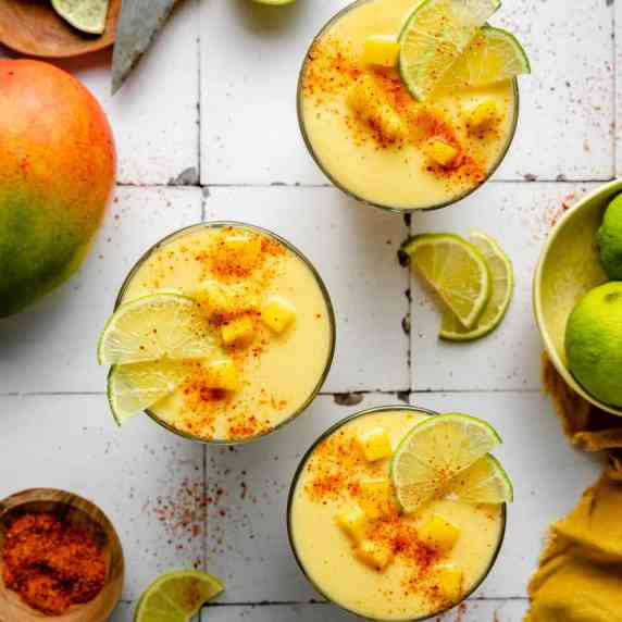 Three glasses of mango pineapple smoothie with tajin, mango and lime on top.
