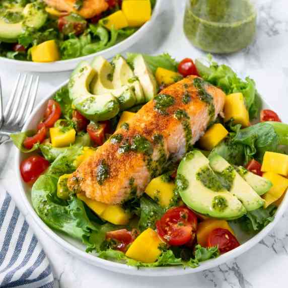 Mango Salmon Salad on a white plate with cilantro lime vinaigrette in the background.