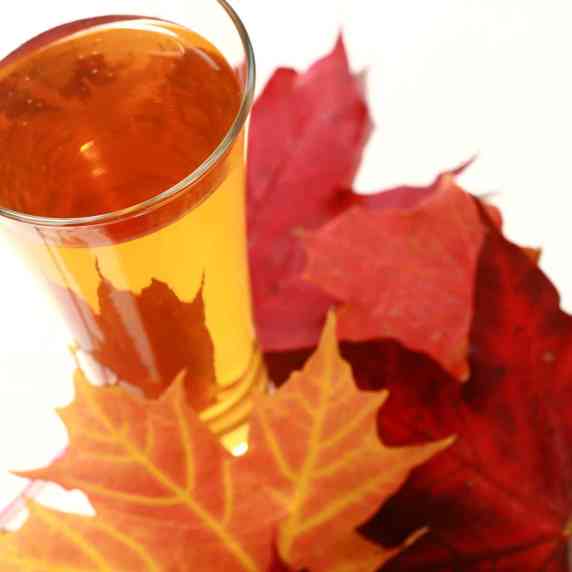 A glass of maple hard apple cider next to colourful maple leaves.