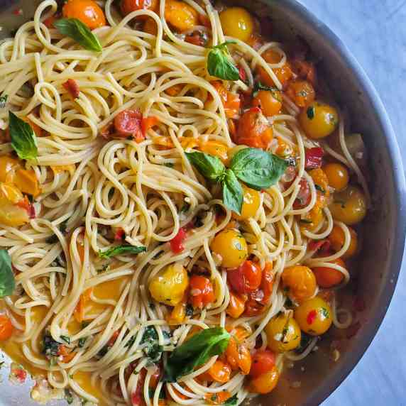 A skillet full of spaghetti and colourful medley cherry tomatoes.