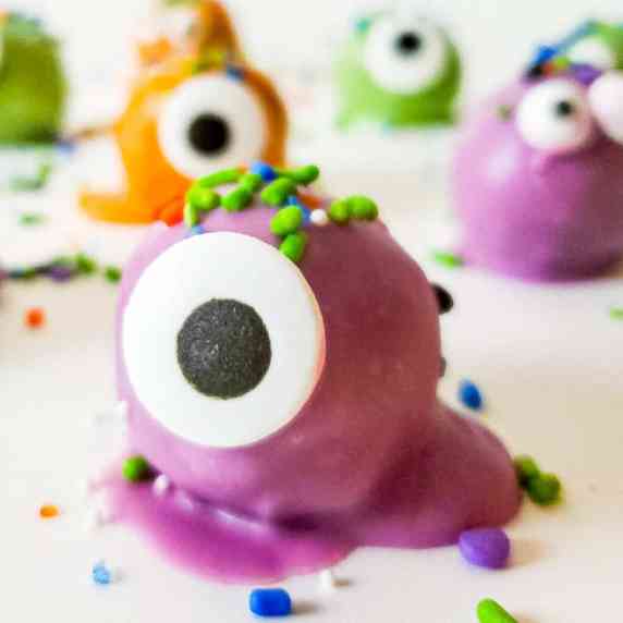 Purple coated truffle decorated with sprinkles and a candy eye with more monster truffles behind.