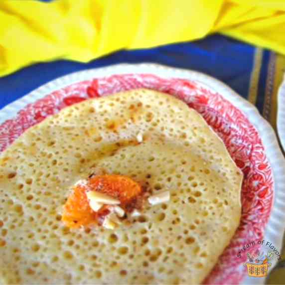 Moroccan pancake on a red plate with almonds, honey, and orange on a blue cloth with a yellow napkin