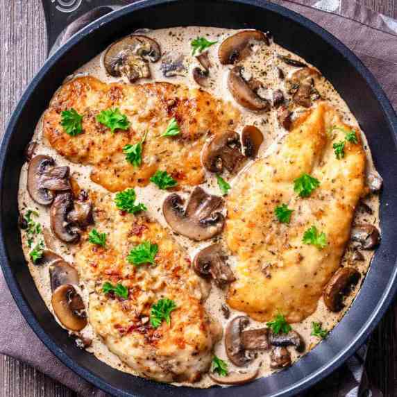 Overhead view of three browned chicken breasts garnished with parsley in a creamy mushroom sauce