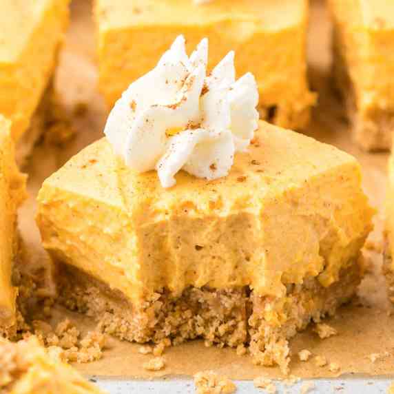 A pumpkin cheesecake bar topped with a swirl of whipped cream on parchment paper.