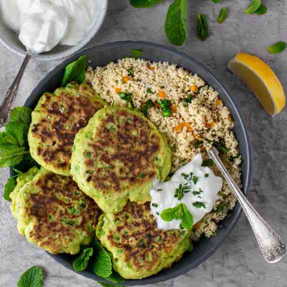 Four pea fritters in a bowl with a portion of couscous. and a dollop of greek yoghurt.