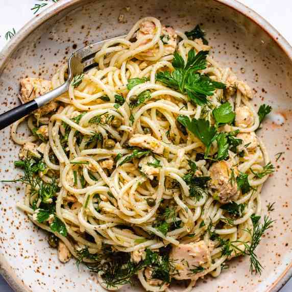 Spaghetti, tuna, capers, and parsley on a plate with a fork 