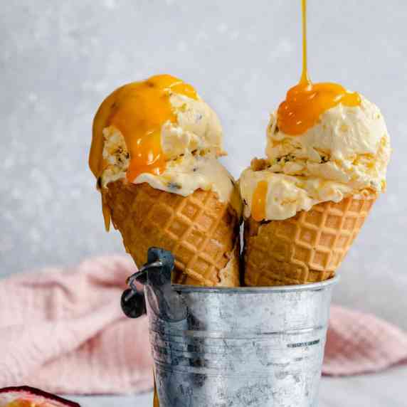 Two passion fruit ice cream cones in a little tin bucket with passion fruit curd being drizzled over