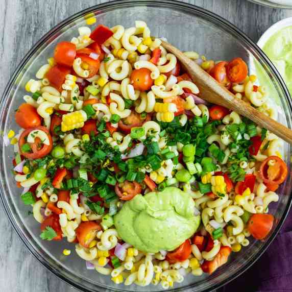 bowl of pasta salad with avocado dressing dollop and green onion and cilantro garnish.