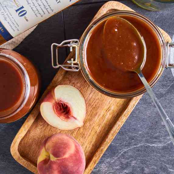 Peach BBQ Sauce with Single Malt in a jar on a wooden board. Surrounded by Talisker and peaches.