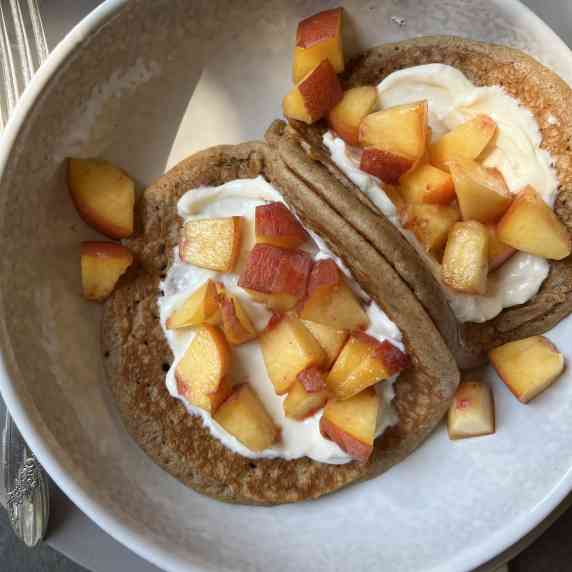 Pancake tacos stuffed with a cream cheese filling and peaches in a beige bowl.  