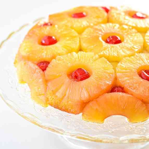 pineapple upside down cake on a glass cake stand on a white table